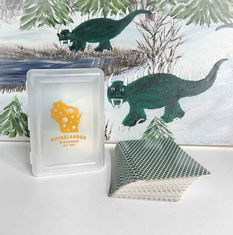 Framed artwork with a hodag painting and 'Rhinelander Wisconsin' logo on a card case and playing cards on a table.