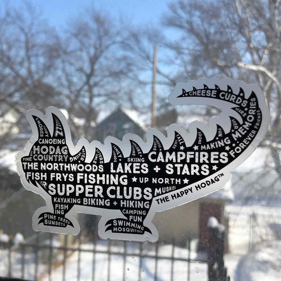 Black Hodag silhouette sticker with white words including 'amores, canoeing, pine trees, fishing, fish frys, up north, lakes+stars, campfires, supper clubs, kayaking, biking + hiking. Sticker shown on a window.